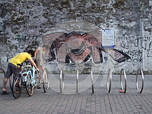 Young couple parking their bicycles in town at a bicycle rack in front of a graffiti wall