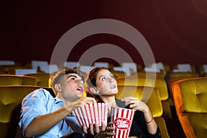 Young couple people watching movie feeling scary and frightening at movie theater. In hand holding snack bucket and throw popcorn