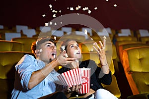 Young couple people watching movie feeling scary and frightening at movie theater. In hand holding snack bucket and throw popcorn