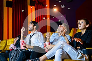 Young couple people watching movie feeling scary and frightening at movie theater. In hand holding snack bucket and throw popcorn