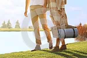 Young couple with picnic basket near lake on sunny day