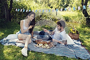 Young couple on a picnic in a city park sitting on a blanket and dueling with skewers with fruits