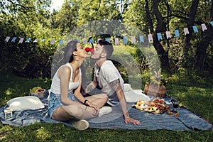 Young couple on a picnic in a city park sitting on a blanket wearing red noses and kissing each other