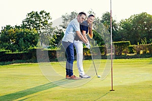 Young couple playing golf. Personal trainer giving lesson on golf course.