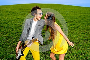 Young couple playing on guitar and enjoying the music, they shout and sing on the green grass background