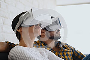 Young Couple Playing Virtual Reality With Headset On Sofa