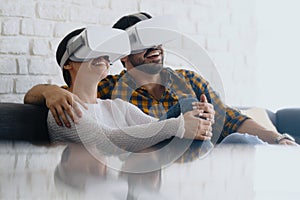 Young Couple Playing Virtual Reality With Headset On Sofa