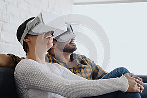 Young Couple Playing Virtual Reality With Headset On Sofa