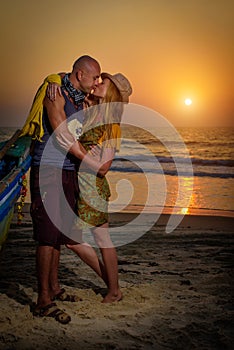 Young couple posing against sea at sunset. Guy and girl fooling and grimace near the old wooden boat on the ocean coast