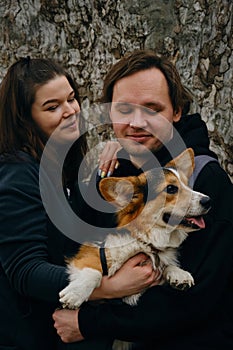 A young couple posing with cute dog welsh corgi pembroke, exchanging loving glances. The dog is perched in the mans arms