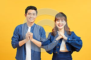 Young couple posing in a yellow background clasping hands at camera in congratulations gesture