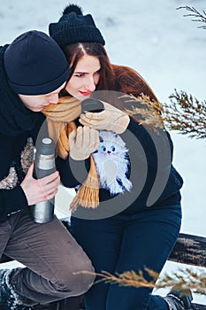 Young couple pours hot tea out of thermos in winter forest