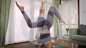 Young couple practicing headstand yoga pose at home. Asian woman and Caucasian man working out and stretching in living