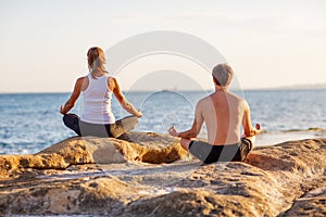 Young couple practicing yoga on the beach at sunset
