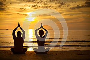 Young couple practicing yoga on beach at sunset