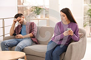 Young couple preferring smartphones over spending time together on couch photo