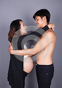 Young couple: pregnant mother and happy father on gray backgroun