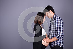 Young couple: pregnant mother and happy father on gray backgroun
