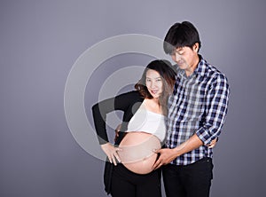 Young couple: pregnant mother and happy father on gray backgroun