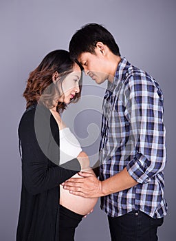 Young couple: pregnant mother and happy father on gray backgroun