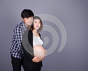 Young couple: pregnant mother and happy father on gray backgroun