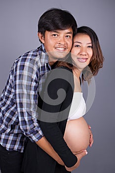 Young couple: pregnant mother and happy father on gray backgroun