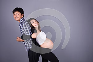 Young couple: pregnant mother and happy father on gray backgroun