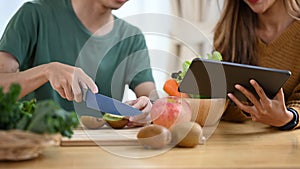 Young couple preparing ingredients for making healthy vegan salad with fresh vegetables in kitchen.