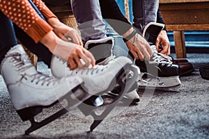 Young couple preparing to a skating. Close-up photo of their hands tying shoelaces of ice hockey skates in the locker