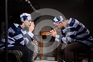 Young couple of prisoners sitting near bedside table and praying photo