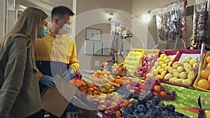 Young couple protective masks and gloves chooses fruits at the market