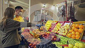 Young couple protective masks and gloves chooses fruits at the market