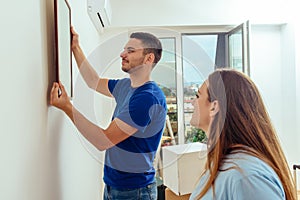 Young Couple Putting Photo Frame On White Wall