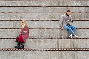 Young couple in a quarrel, a guy and a girl are sitting far from each other in the empty stands