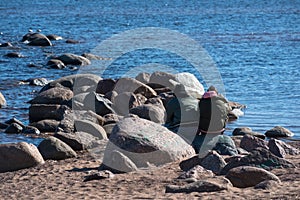 Young couple, quite fat man and woman, wearing jackets with hoods and hats sit next to each other on the grey rock on the rocky