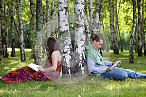 Young couple reading books in park by tree trunk