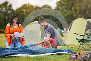 Young Couple Reading Instructions For Putting Up Tent At Summer Music Festival Unpacking Equipment