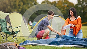 Young Couple Reading Instructions For Putting Up Tent At Summer Music Festival Unpacking Equipment