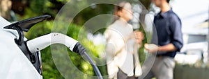 Young couple recharge electric car's battery from charging station. Expedient