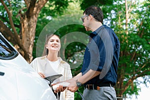 Young couple recharge electric car's battery from charging station. Expedient