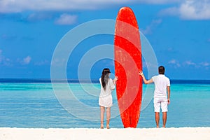 Young couple with red surfboard on white beach