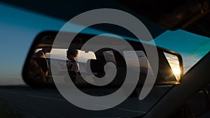 Young couple in reflection of auto mirror, look at map at sunset near road