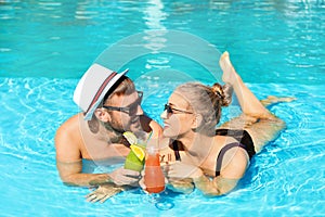 Young couple with refreshing cocktails in swimming pool