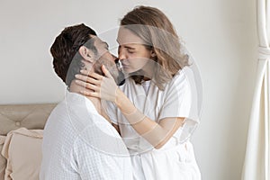 Young couple in a relationship kissing and cuddling. Happy couple hug and kiss on the bed near the window in the morning.