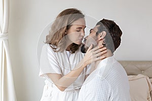 Young couple in a relationship kissing and cuddling. Happy couple hug and kiss on the bed near the window in the morning.