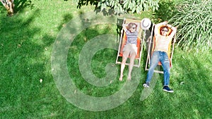 Young couple relax in summer garden in sunbed deckchairs on grass, woman and men outdoors, aerial top view