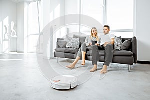 Young couple relaxing while automatic vacuum cleaner working at home