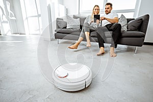 Young couple relaxing while automatic vacuum cleaner working at home
