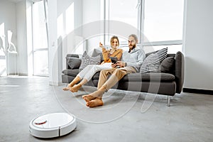 Young couple relaxing while automatic vacuum cleaner working at home