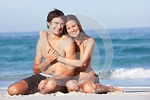 Young Couple Relaxing On Beach Wearing Swimwear